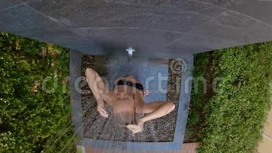 一个年轻女人在热带花园里洗澡的慢镜头。 在热带<strong>度假</strong>胜地<strong>度假</strong>的概念。 年轻女子